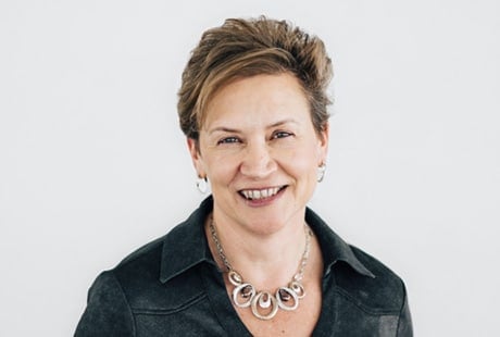 Smiling person with short hair, wearing a necklace and black top, against a white background.
