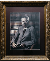 Framed portrait of an elderly man in suit sitting in front of bookshelves, conveying wisdom and authority.