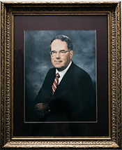 Portrait of a man in a suit and red tie, framed in an ornate, golden frame with a dark background.