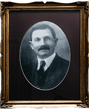 Vintage portrait of a man with a mustache in an ornate frame, wearing a suit and tie, black and white photo.