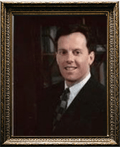 Portrait of a smiling person in a suit, framed in an ornate brown and gold frame.
